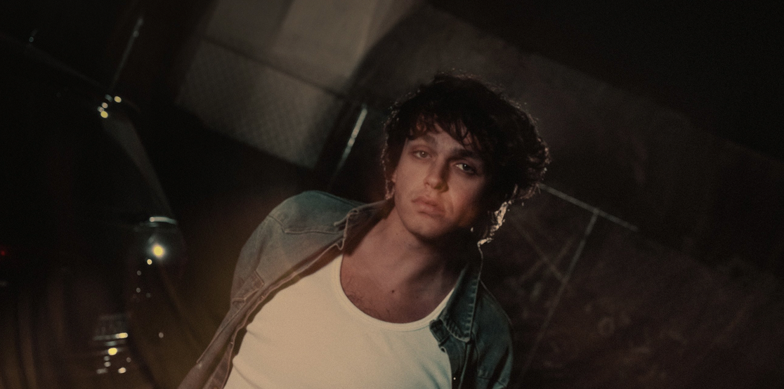 a man with a white short laying down tilted to the right side. The background is dark